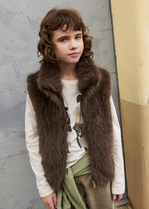 Girl wearing Mayoral dark olive faux fur gilet over white graphic long-sleeve tee – on model front view
