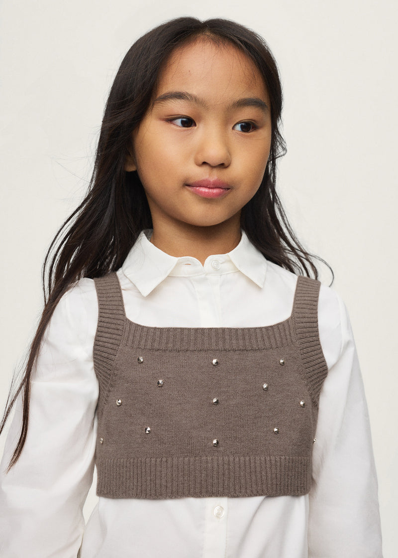 Girl wearing Mayoral cream shirt with black rhinestone knit vest layered over – on model full body view