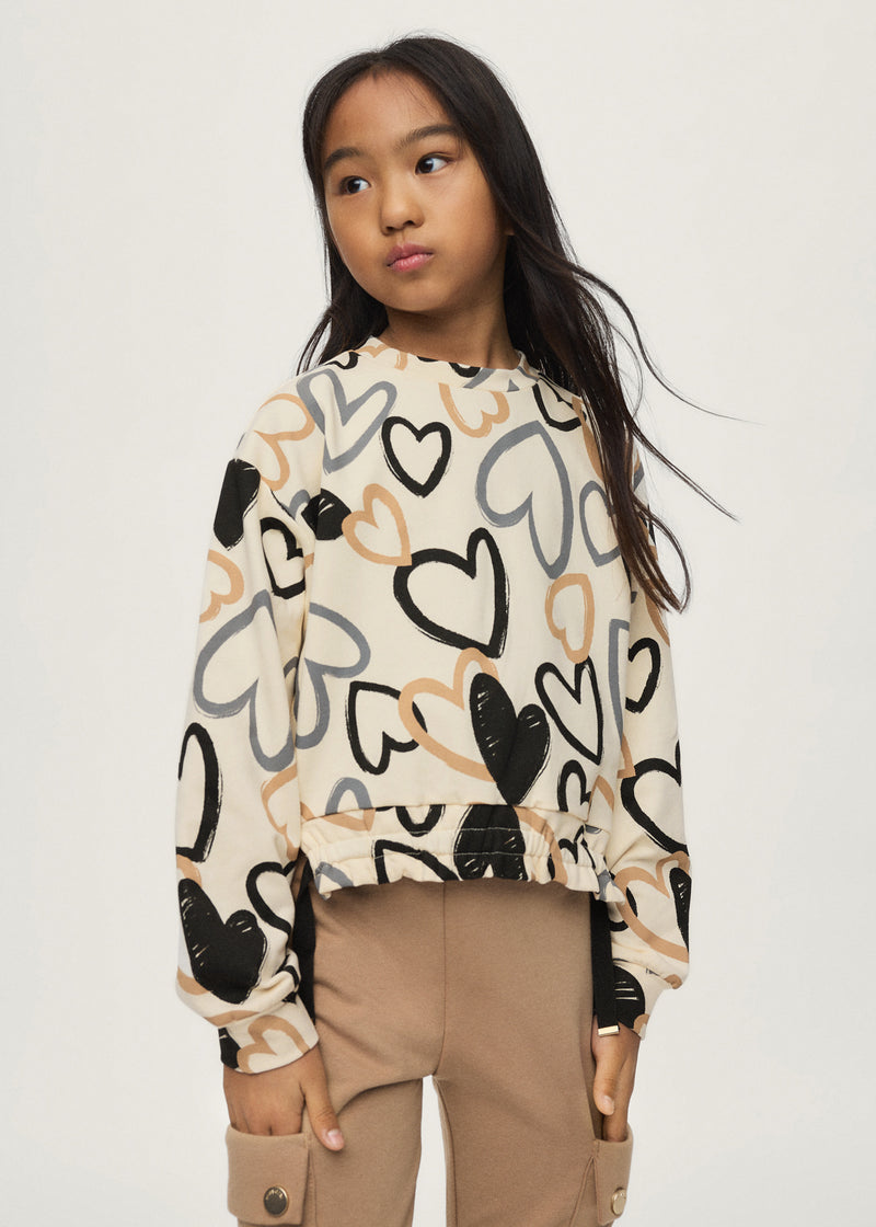 Girl wearing Mayoral all-over heart print sweatshirt styled with camel cargo trousers – on model full body front view