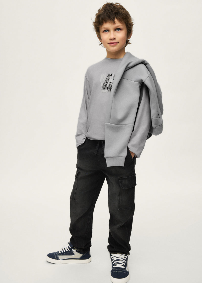Boy wearing Mayoral Nukutavake black cargo trousers with grey graphic sweatshirt and Vans – on model full body front view