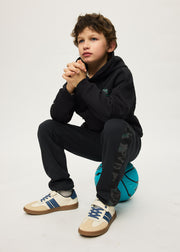 Boy sitting on basketball wearing Mayoral Nukutavake black camo joggers – showing tonal camo side panel detail on leg